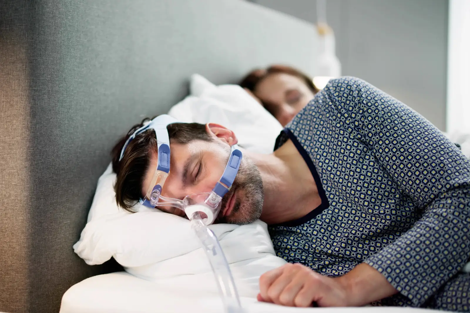 Homme dormant avec un masque CPAP pour traiter l’apnée du sommeil, aux côtés de sa partenaire.