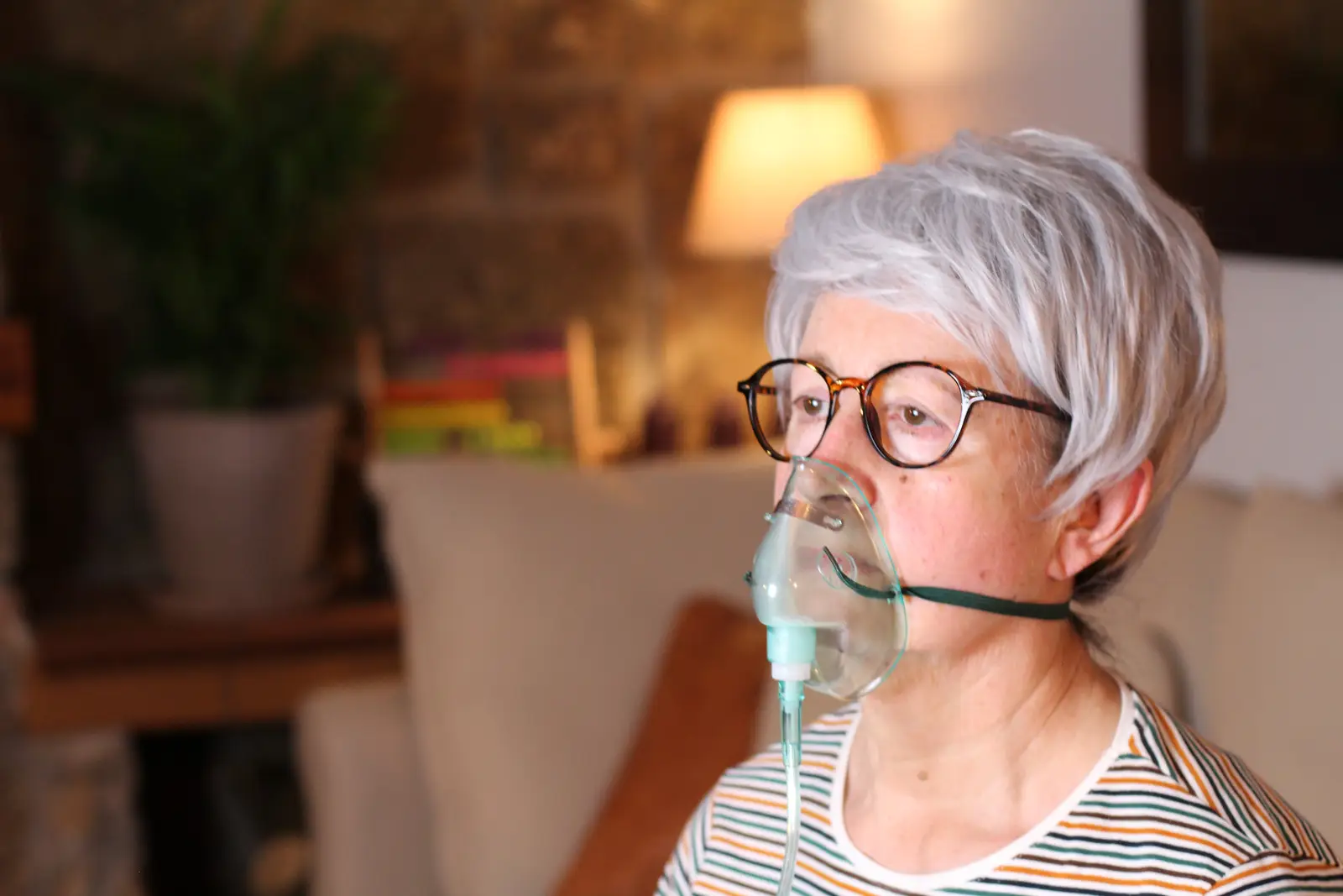 Femme portant un masque à oxygène chez elle, recevant un traitement d'oxygénothérapie pour des problèmes respiratoires.